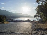 a man is riding his skateboard on the road near the water and mountains during a sunny day