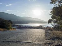 a man is riding his skateboard on the road near the water and mountains during a sunny day