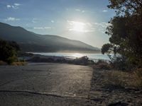 a man is riding his skateboard on the road near the water and mountains during a sunny day