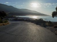 a man is riding his skateboard on the road near the water and mountains during a sunny day
