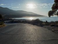 a man is riding his skateboard on the road near the water and mountains during a sunny day
