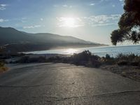 a man is riding his skateboard on the road near the water and mountains during a sunny day