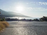 a man is riding his skateboard on the road near the water and mountains during a sunny day