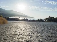 a man is riding his skateboard on the road near the water and mountains during a sunny day