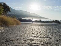 a man is riding his skateboard on the road near the water and mountains during a sunny day