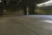 a man on a skateboard riding through an empty park underneath an overpass with trees