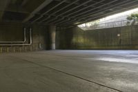 a man on a skateboard riding through an empty park underneath an overpass with trees