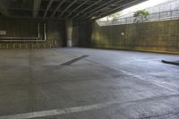 a man on a skateboard riding through an empty park underneath an overpass with trees