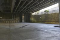 a man on a skateboard riding through an empty park underneath an overpass with trees