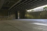 a man on a skateboard riding through an empty park underneath an overpass with trees