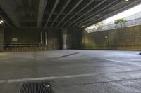 a man on a skateboard riding through an empty park underneath an overpass with trees