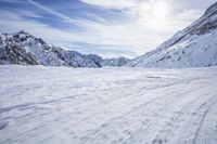 a man skiing down a snowy mountain path, with the sun behind him and clouds overhead