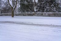 a man snow skiing down a snow covered road by a wooded area next to a fence