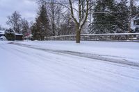 a man snow skiing down a snow covered road by a wooded area next to a fence