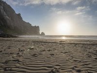 there is a man standing on the beach near some rocks and water behind him are a lot of footprints