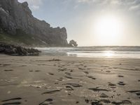 there is a man standing on the beach near some rocks and water behind him are a lot of footprints