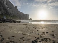 there is a man standing on the beach near some rocks and water behind him are a lot of footprints