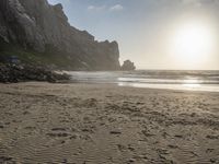 there is a man standing on the beach near some rocks and water behind him are a lot of footprints