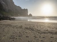 there is a man standing on the beach near some rocks and water behind him are a lot of footprints