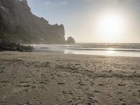 there is a man standing on the beach near some rocks and water behind him are a lot of footprints