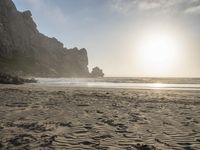 there is a man standing on the beach near some rocks and water behind him are a lot of footprints