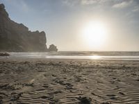 there is a man standing on the beach near some rocks and water behind him are a lot of footprints