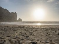 there is a man standing on the beach near some rocks and water behind him are a lot of footprints