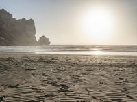 there is a man standing on the beach near some rocks and water behind him are a lot of footprints