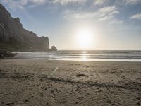 there is a man standing on the beach near some rocks and water behind him are a lot of footprints