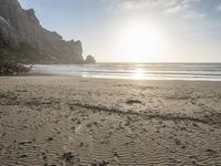 there is a man standing on the beach near some rocks and water behind him are a lot of footprints