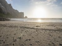 there is a man standing on the beach near some rocks and water behind him are a lot of footprints