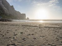 there is a man standing on the beach near some rocks and water behind him are a lot of footprints