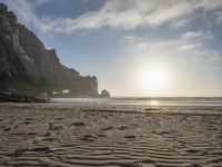 there is a man standing on the beach near some rocks and water behind him are a lot of footprints