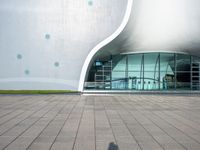 a man in shorts is standing on the walkway with a skateboard, in front of the modern building with large windows