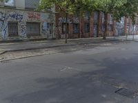 the man stands near the fire hydrant in front of the building and trees with graffiti on it