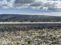 a man stands on a road in the mountains above some barren land and there is only a hill in the distance