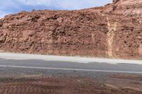 man standing on the side of the road next to rocks with a motorcycle on the side