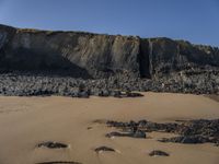 a man standing on top of a sandy beach under a cliff next to the ocean