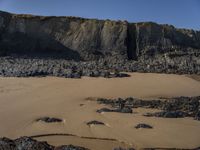 a man standing on top of a sandy beach under a cliff next to the ocean