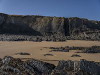 a man standing on top of a sandy beach under a cliff next to the ocean