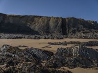 a man standing on top of a sandy beach under a cliff next to the ocean