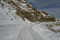 the path has lots of tracks going through it in the snow and on the rocks there is a man standing on a steep mountain