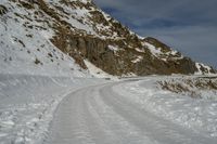 the path has lots of tracks going through it in the snow and on the rocks there is a man standing on a steep mountain