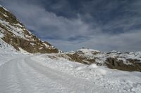 the path has lots of tracks going through it in the snow and on the rocks there is a man standing on a steep mountain