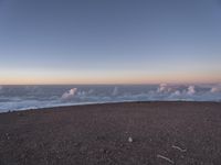 a lone man standing at the top of a hill and looking at the clouds below him