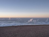 a lone man standing at the top of a hill and looking at the clouds below him