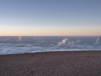 a lone man standing at the top of a hill and looking at the clouds below him