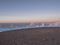 a lone man standing at the top of a hill and looking at the clouds below him