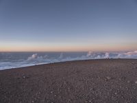 a lone man standing at the top of a hill and looking at the clouds below him