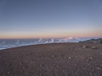 a lone man standing at the top of a hill and looking at the clouds below him